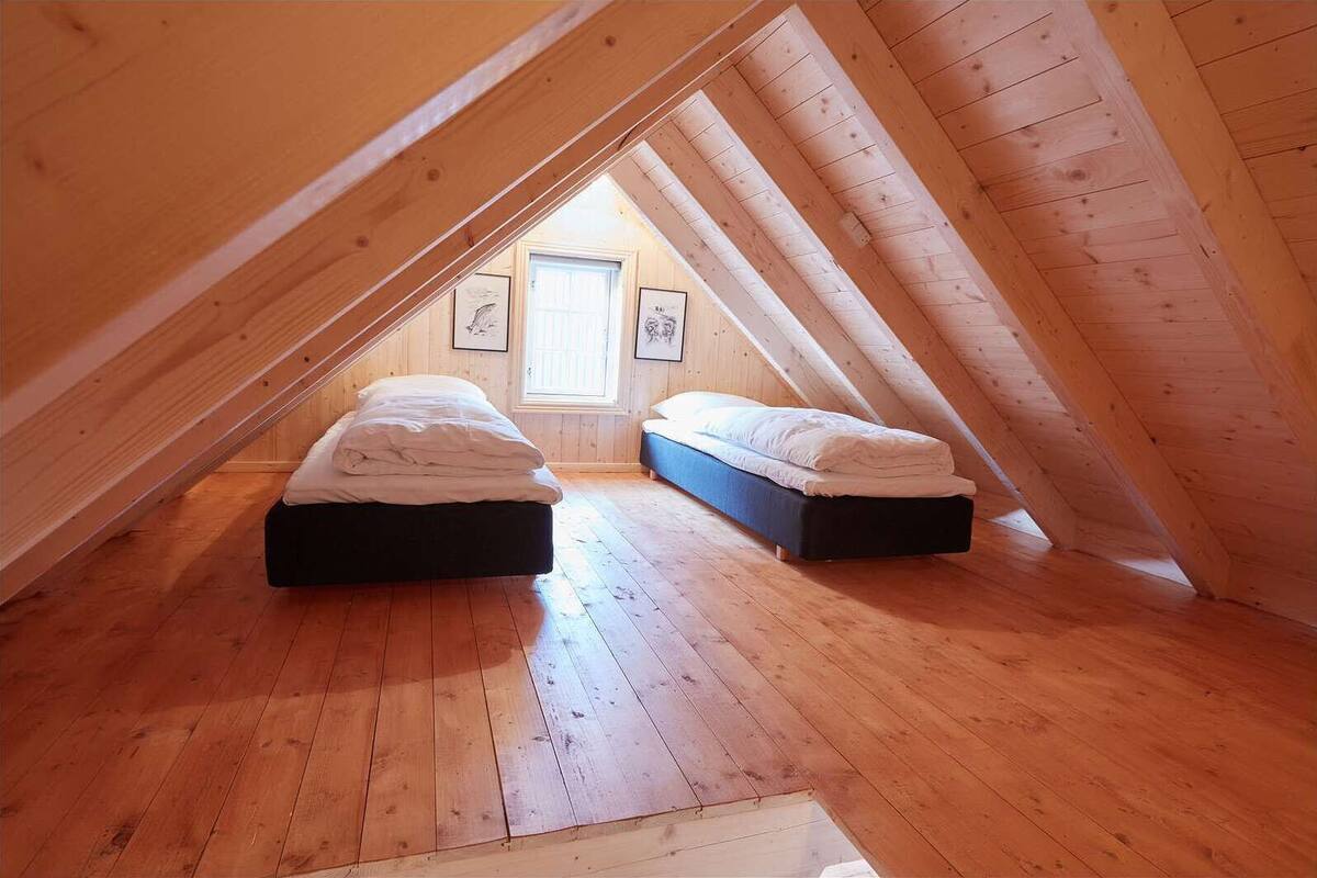 Une petite chambre mansardée avec deux lits, un plancher en bois et un plafond en pente.