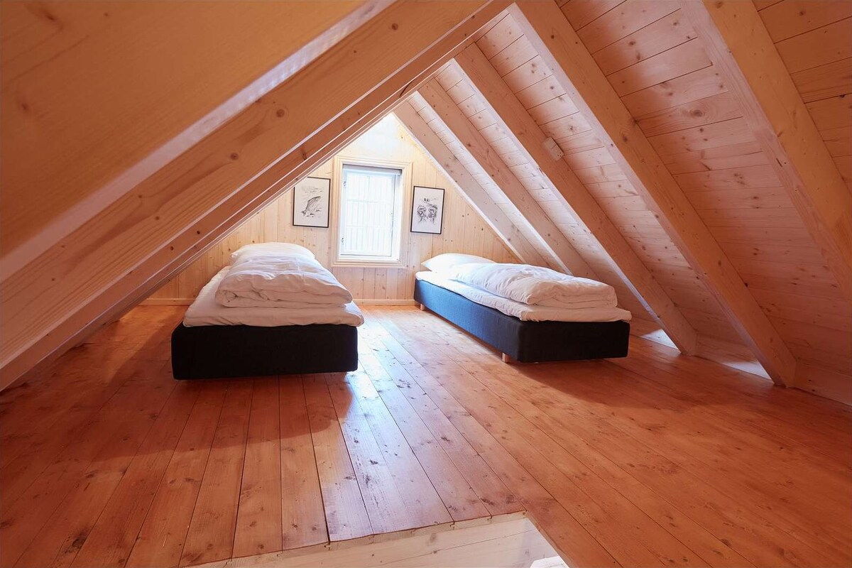 Un pequeño dormitorio en el ático con dos camas, pisos de madera y techo inclinado.