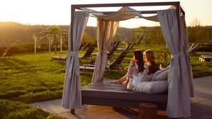 A bed with a canopy in an outdoor setting with lounge chairs in the background. - Bio-Seehotel Zeulenroda (Zeulenroda-Triebes)