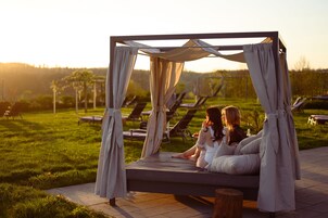 A bed with a canopy in an outdoor setting with lounge chairs in the background.