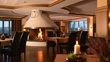 A dining area with a fireplace, wooden ceiling, and large windows.