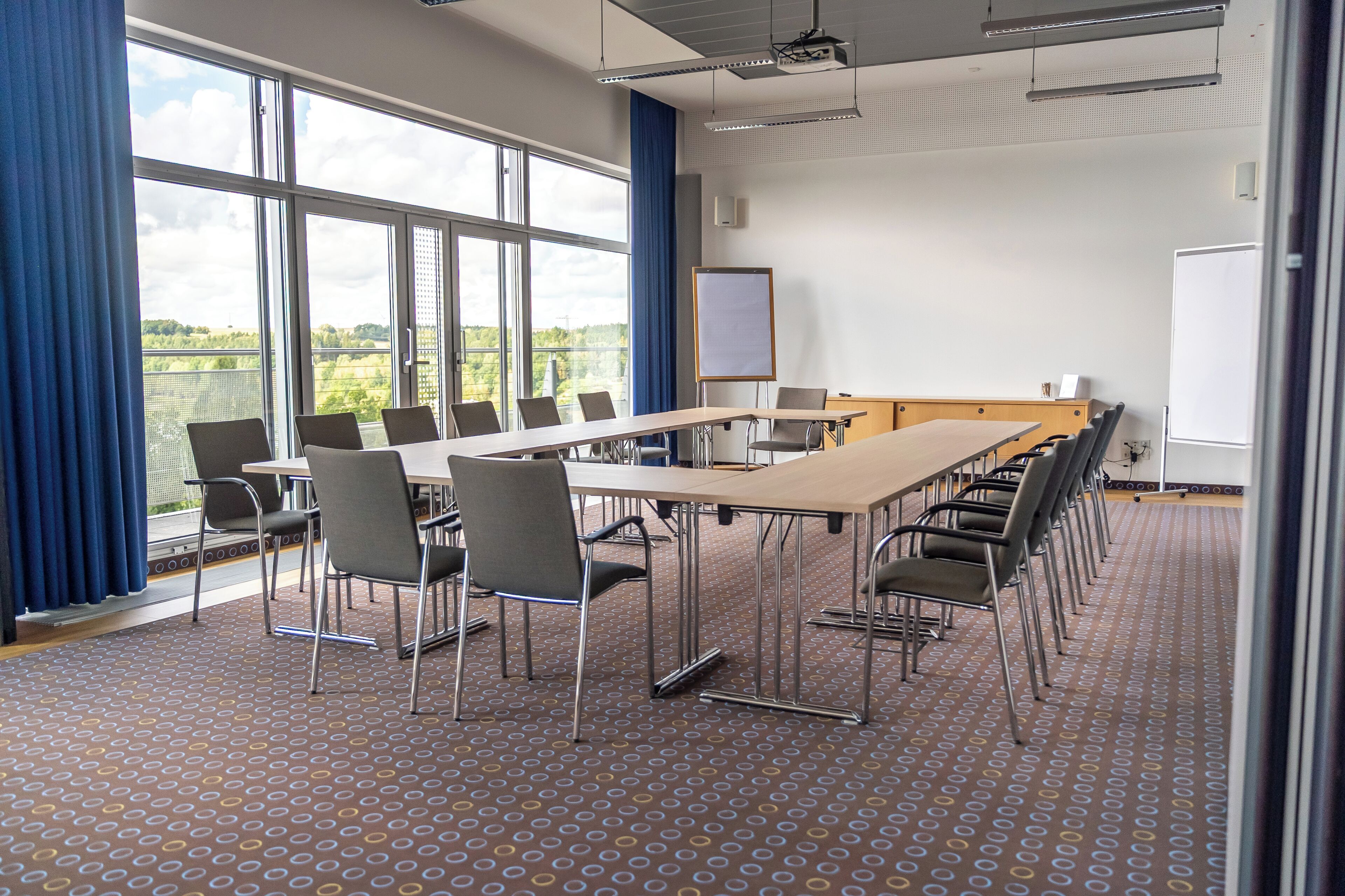 Un salón de conferencias con una mesa larga, sillas, una pizarra blanca y ventanas amplias.