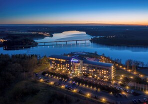 A hotel with a large parking lot, a bridge in the background, and a body of water. - Bio-Seehotel Zeulenroda (Zeulenroda-Triebes)