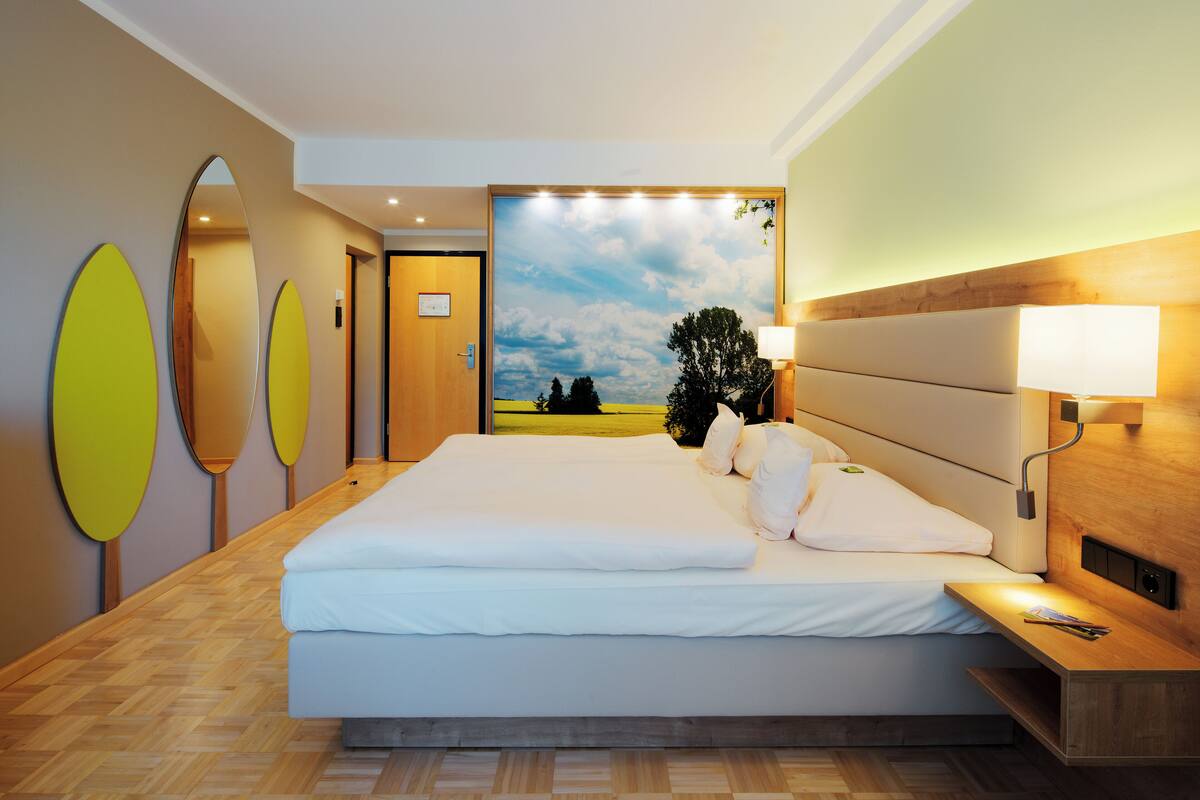 A hotel room with a large bed, a wooden headboard, a nightstand, and a wall-mounted lamp.