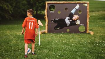 A child in a red soccer uniform with the number 11, standing on a grassy field with a soccer goal in the background.