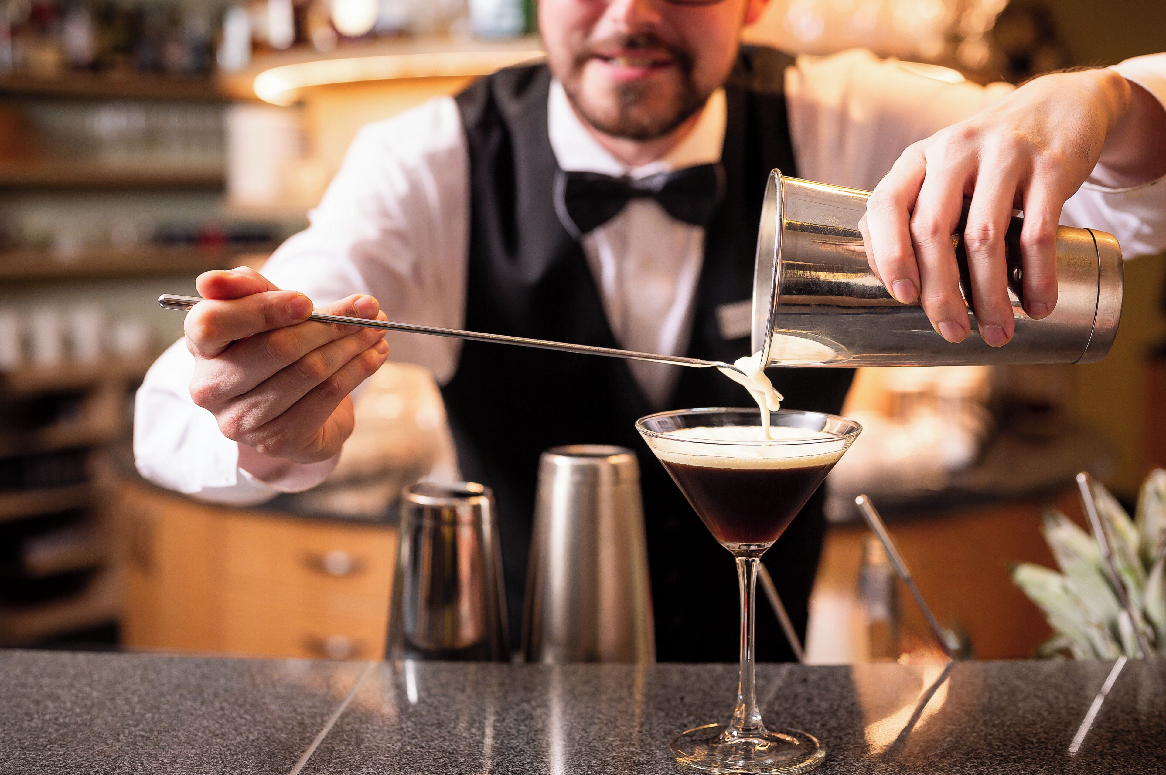 En bartender som häller upp en drink i ett martiniglas.