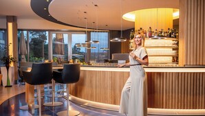 A modern bar area with a curved counter, bar stools, and a woman standing by the bar. - Bio-Seehotel Zeulenroda (Zeulenroda-Triebes)