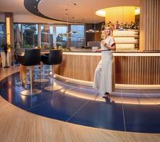 A modern bar area with a curved counter, bar stools, and a woman standing by the bar.