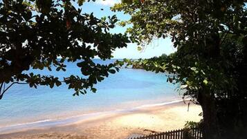 A beach with a wooden fence and trees in the foreground.