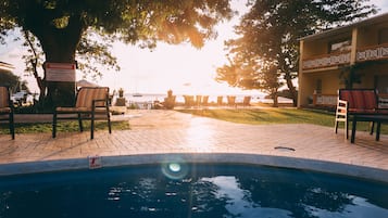 A pool area with chairs and a warning sign, a building with a balcony, and a view of the sea.