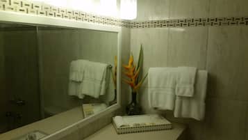 A bathroom with a large mirror, two white towels hanging on the wall, a vase with a plant, and a small tray with toiletries.