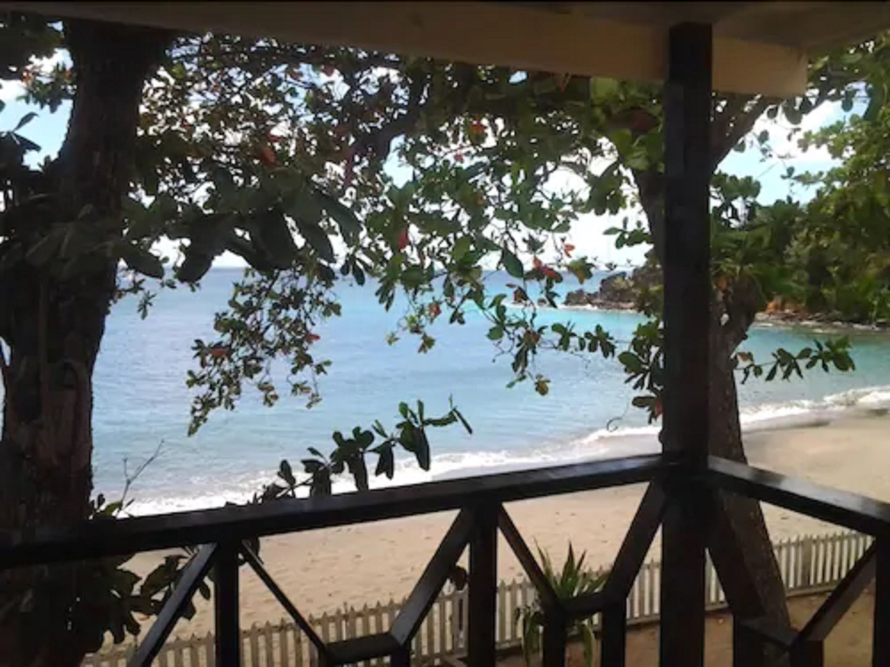 A beach view from a covered area with a wooden railing and trees.