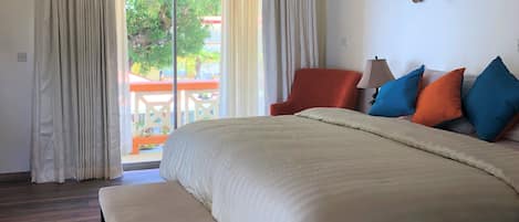 A hotel room with a large bed, a bench, a chair, and a table with a lamp.