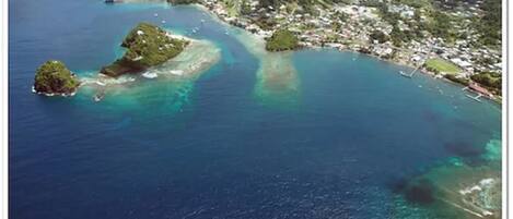 An aerial view of a coastal area with clear blue waters, several small islands, and a densely populated town with visible buildings and infrastructure.