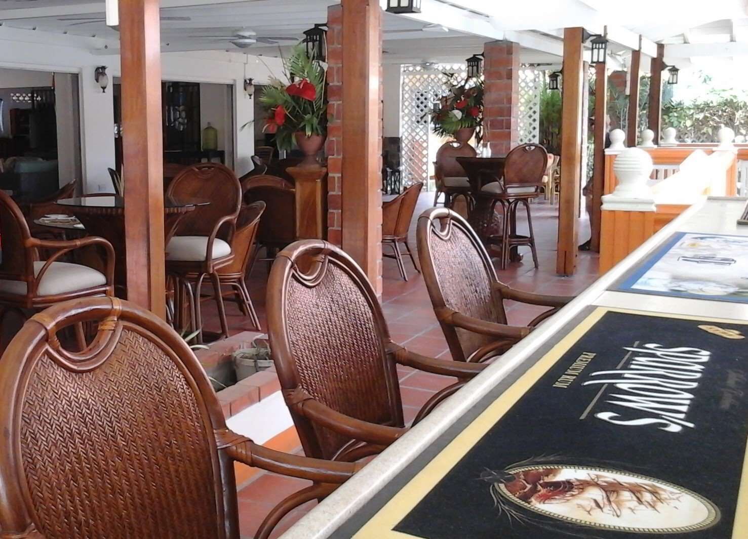 A restaurant with wicker chairs, a long table with a menu, and a brick pillar.