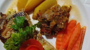 A plate with a piece of grilled fish, potatoes, carrots, and a garnish of parsley and a red flower.