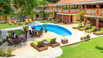 A resort with a swimming pool, outdoor seating, and a covered area with a view of the pool.
