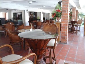 A covered outdoor dining area with wicker chairs and a glass table, brick pillars, and potted plants. - Sunset Shores Beach Hotel (Villa)