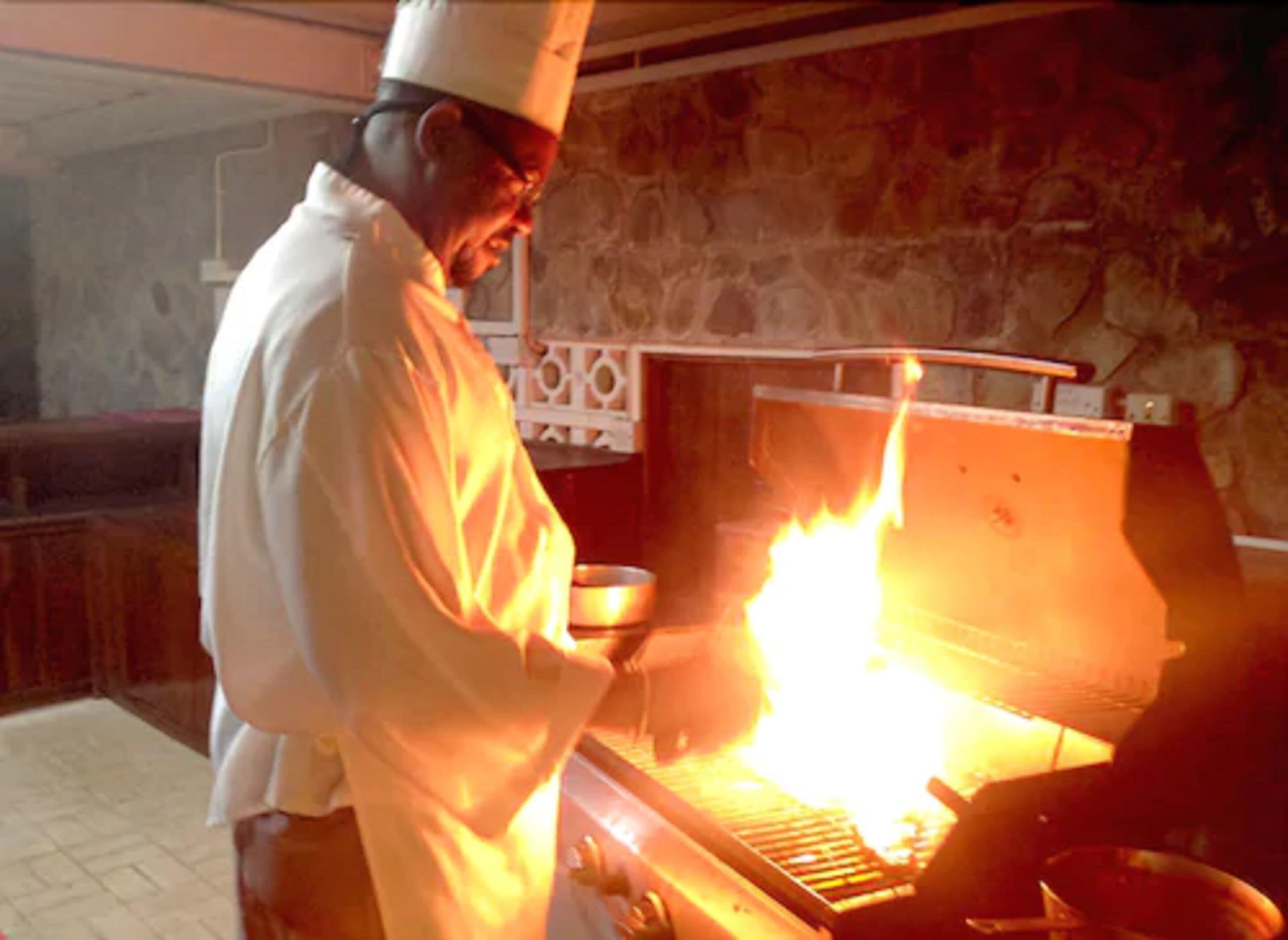 Um cozinheiro com uniforme branco cozinha usando uma chama alta.