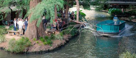 Un río con una barca, gente sentada en un banco y un puente al fondo.