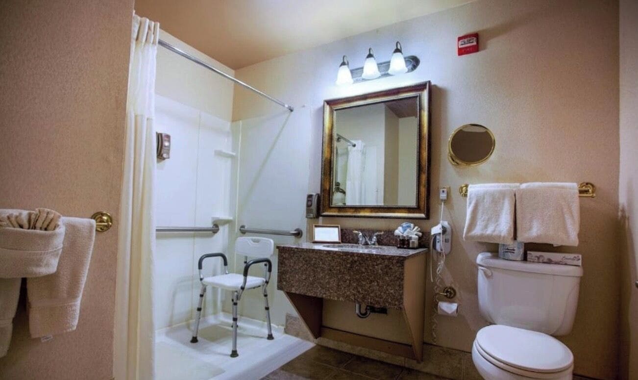 Un baño con ducha, lavamanos, inodoro y una silla accesible para sillas de ruedas.