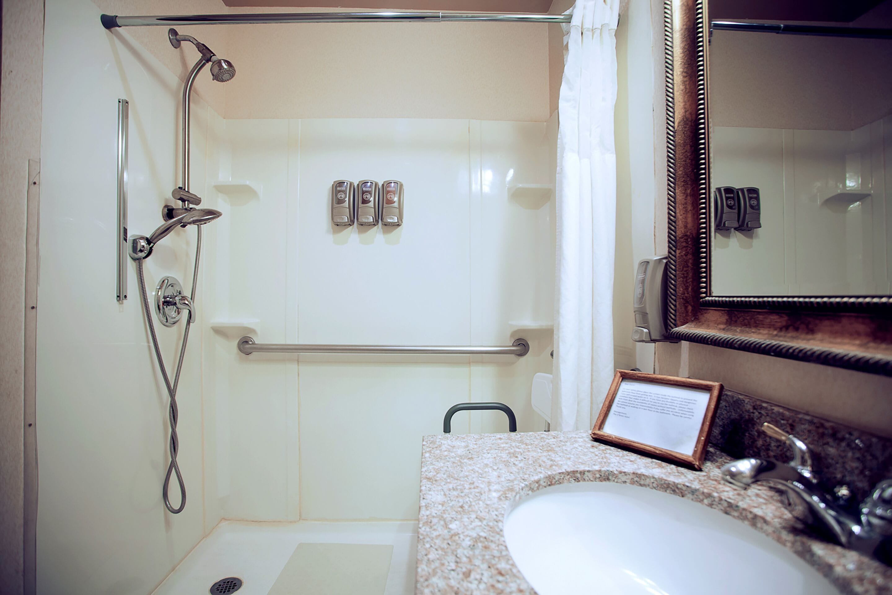A bathroom with a shower, grab bar, sink, and mirror.