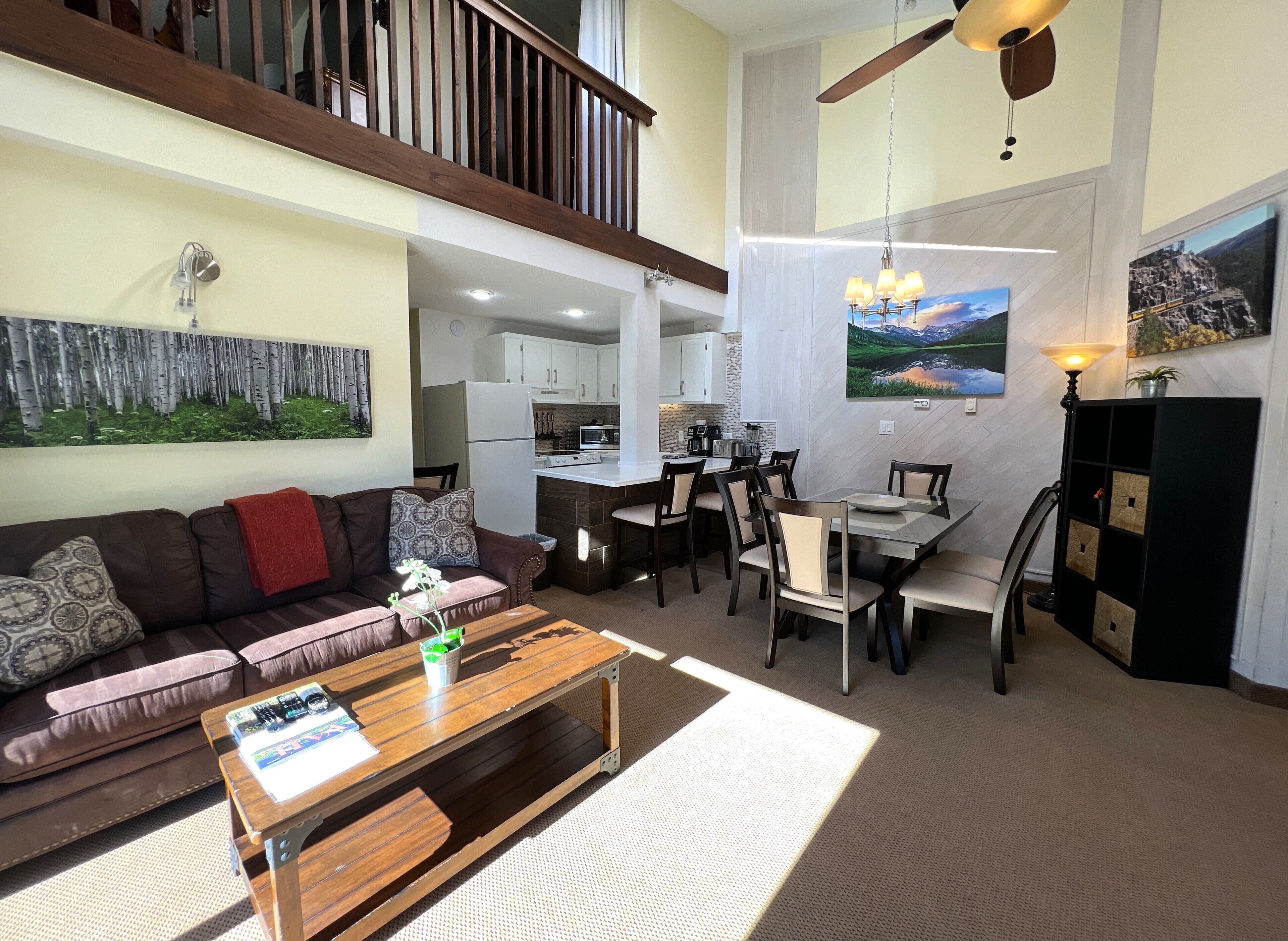 A spacious living area with a sofa, coffee table, and dining table set. A kitchen is visible in the background, and a balcony with a railing is present.