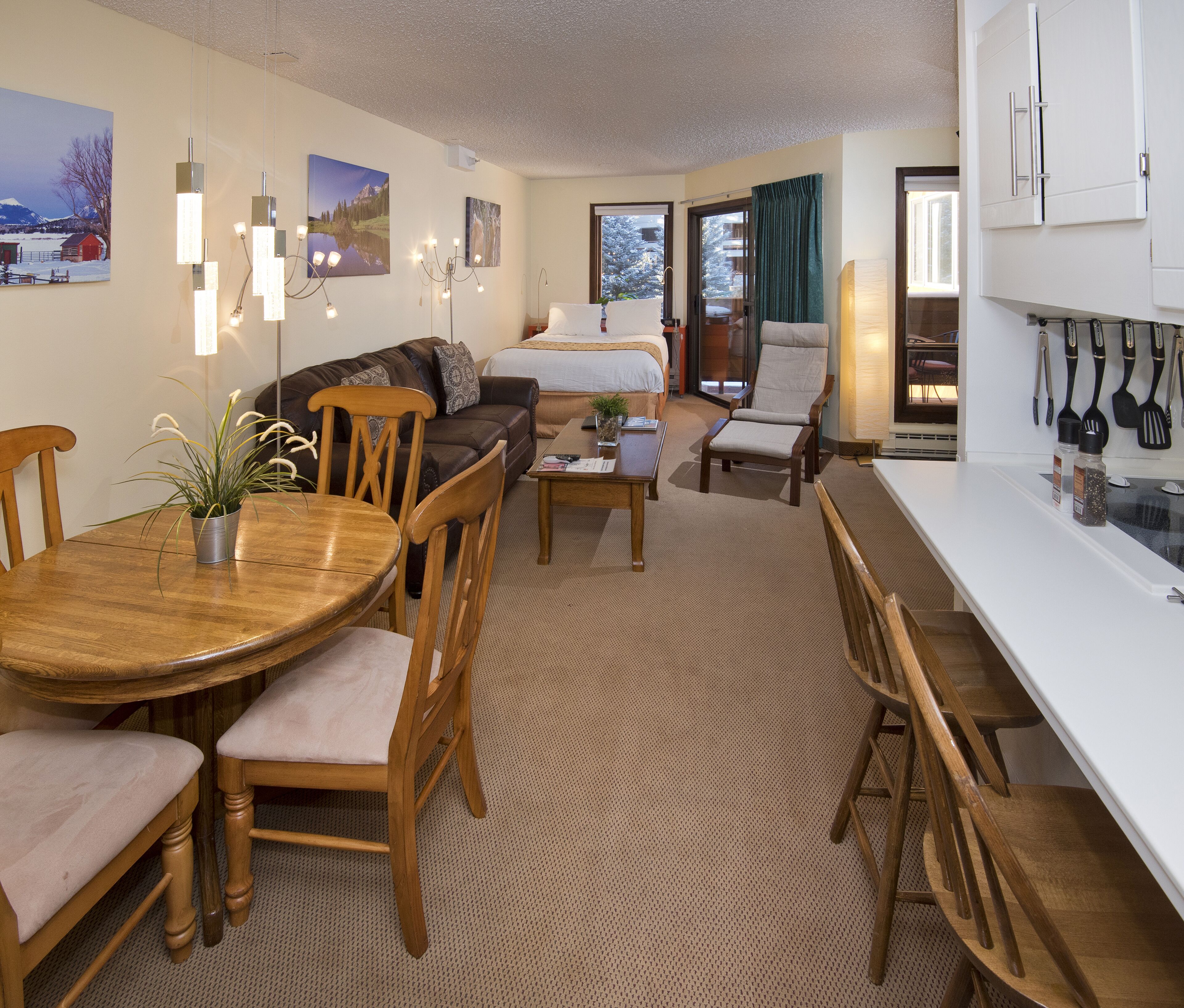 A modern hotel room with a dining area, a sofa, a bed, and a kitchen area.
