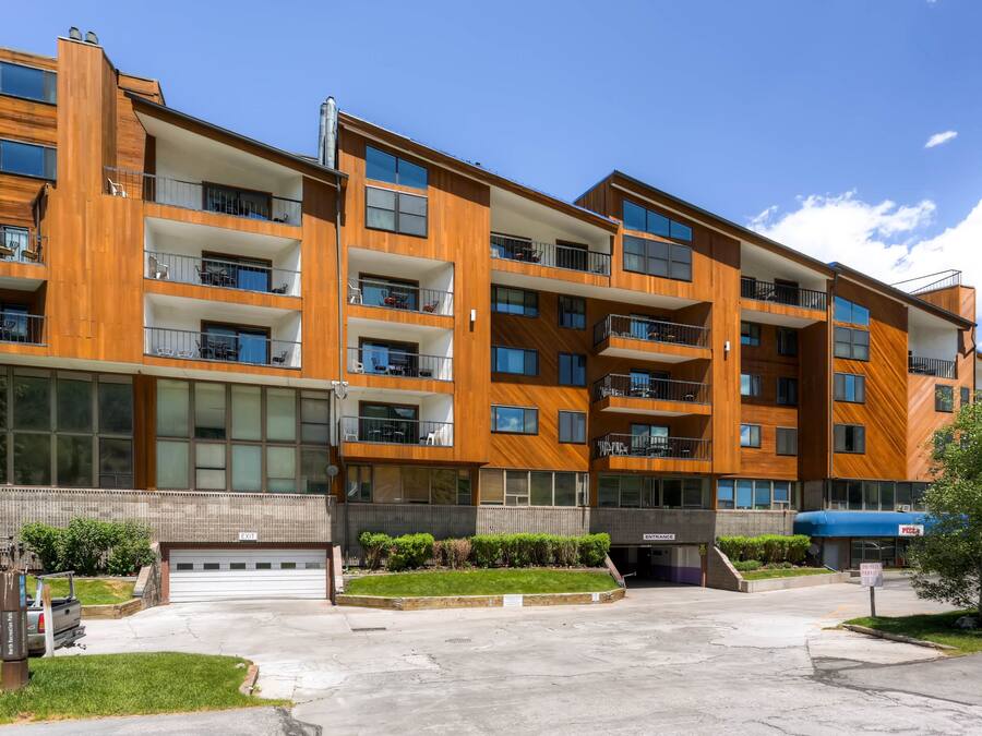 A multi-story residential building with balconies, large windows, and a parking area.