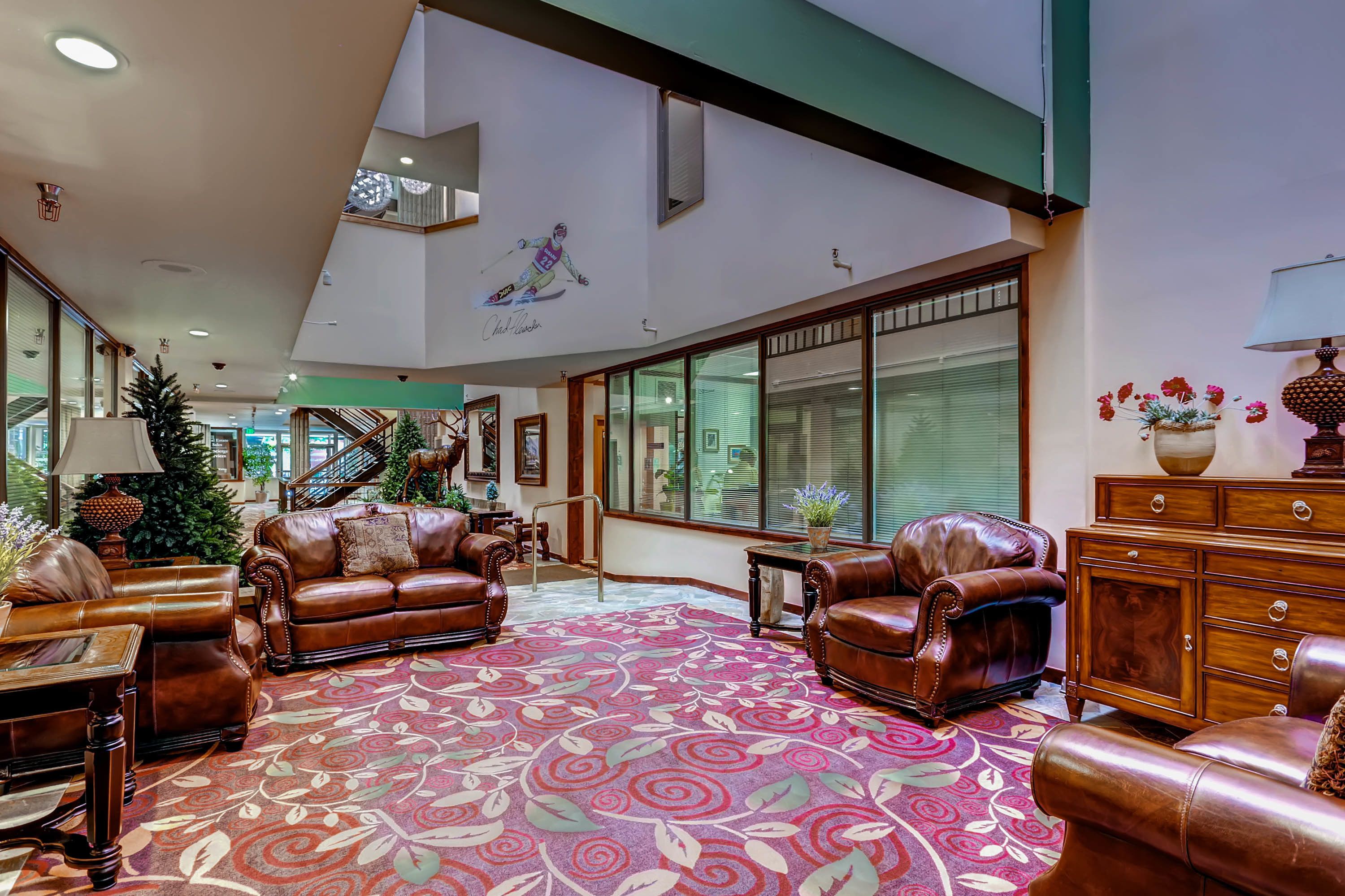 Eine großzügige Lobby mit Ledersofas, einem gemusterten Teppich und einem großen Fenster mit Jalousien.