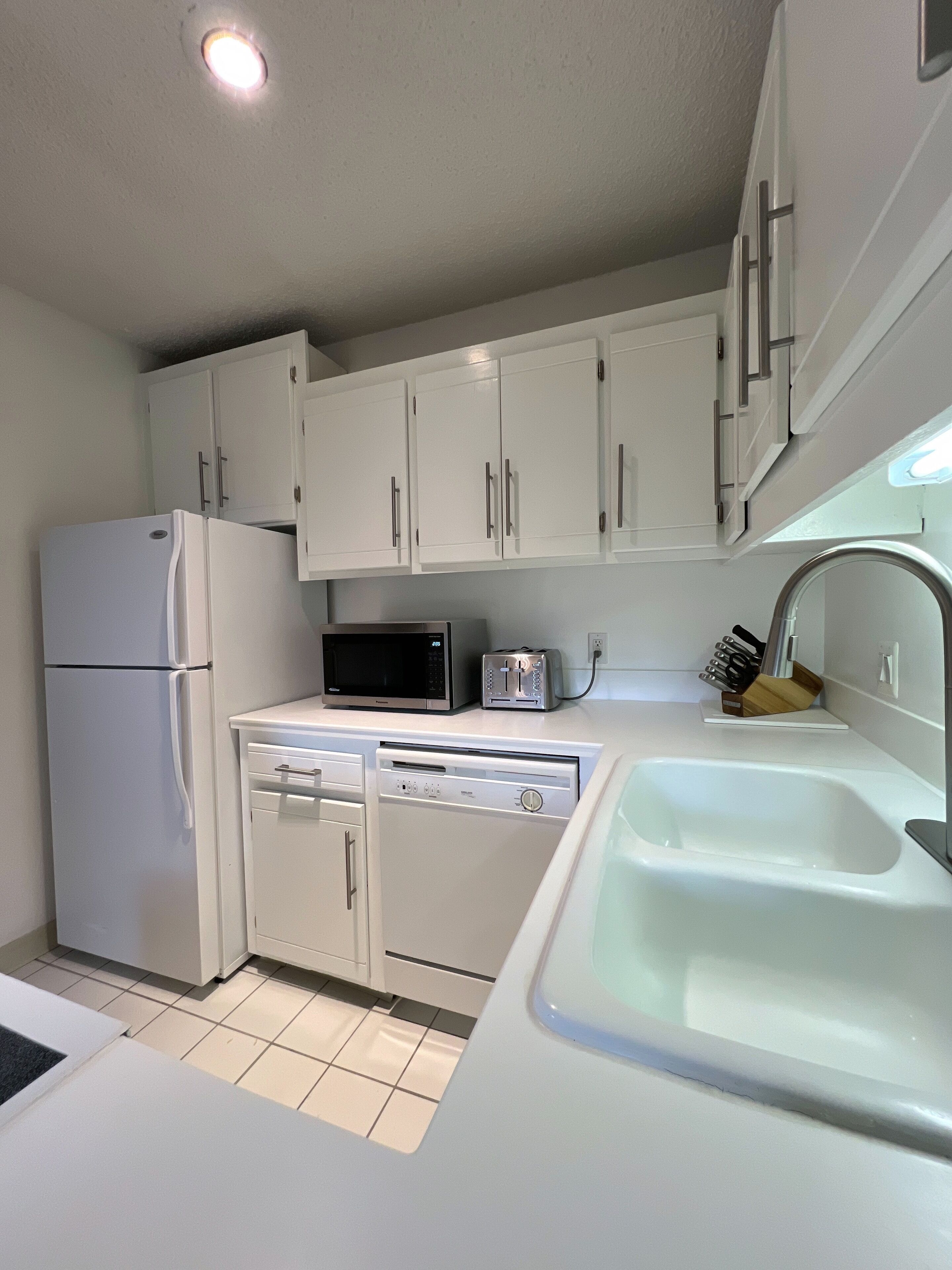 A kitchen with white cabinets, a refrigerator, a microwave, a toaster, and a sink.
