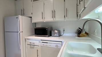 A kitchen with white cabinets, a refrigerator, a microwave, a toaster, and a sink.