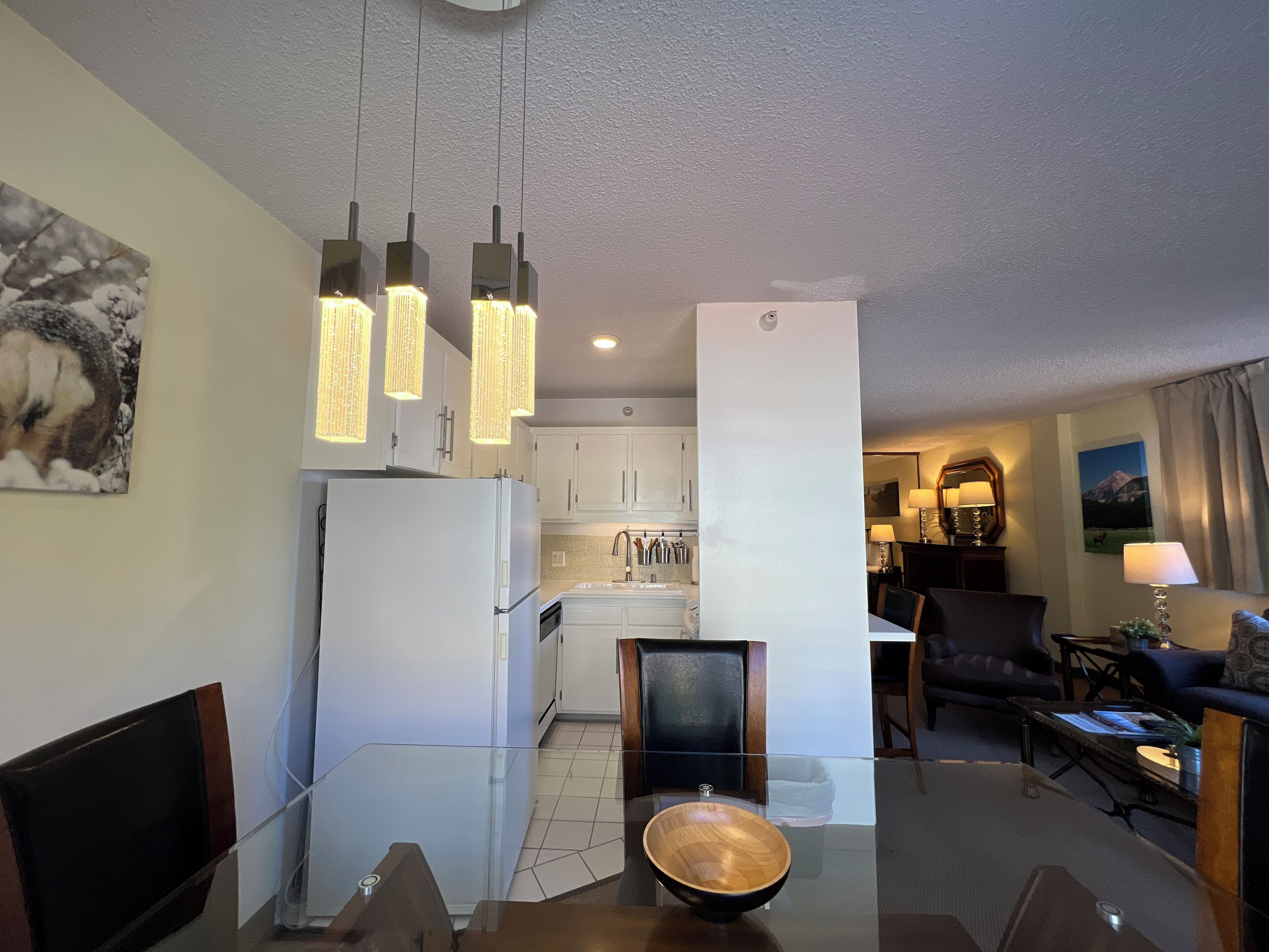 Una sala de estar moderna con una mesa de comedor, una cocina al fondo y un cuadro grande en la pared.