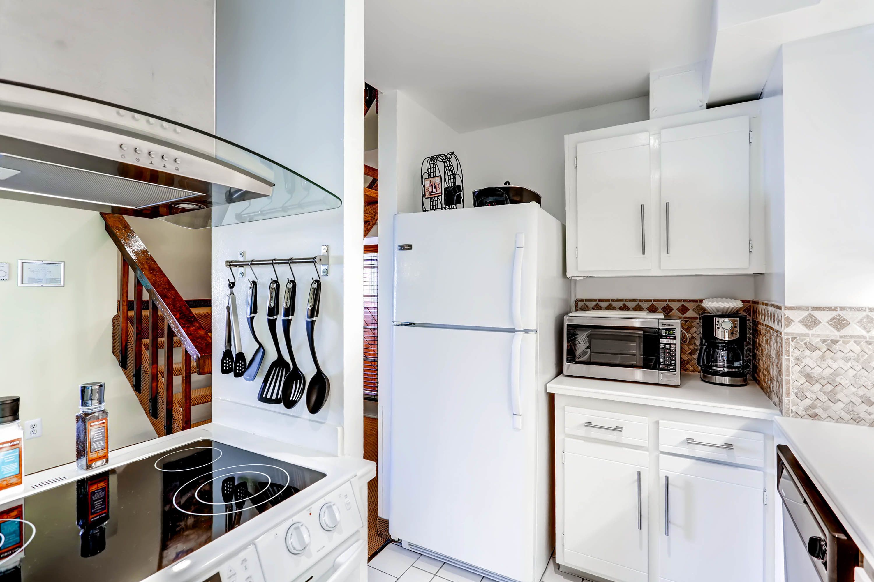 Una cocina compacta con estufa, microondas, refrigerador y gabinetes blancos.