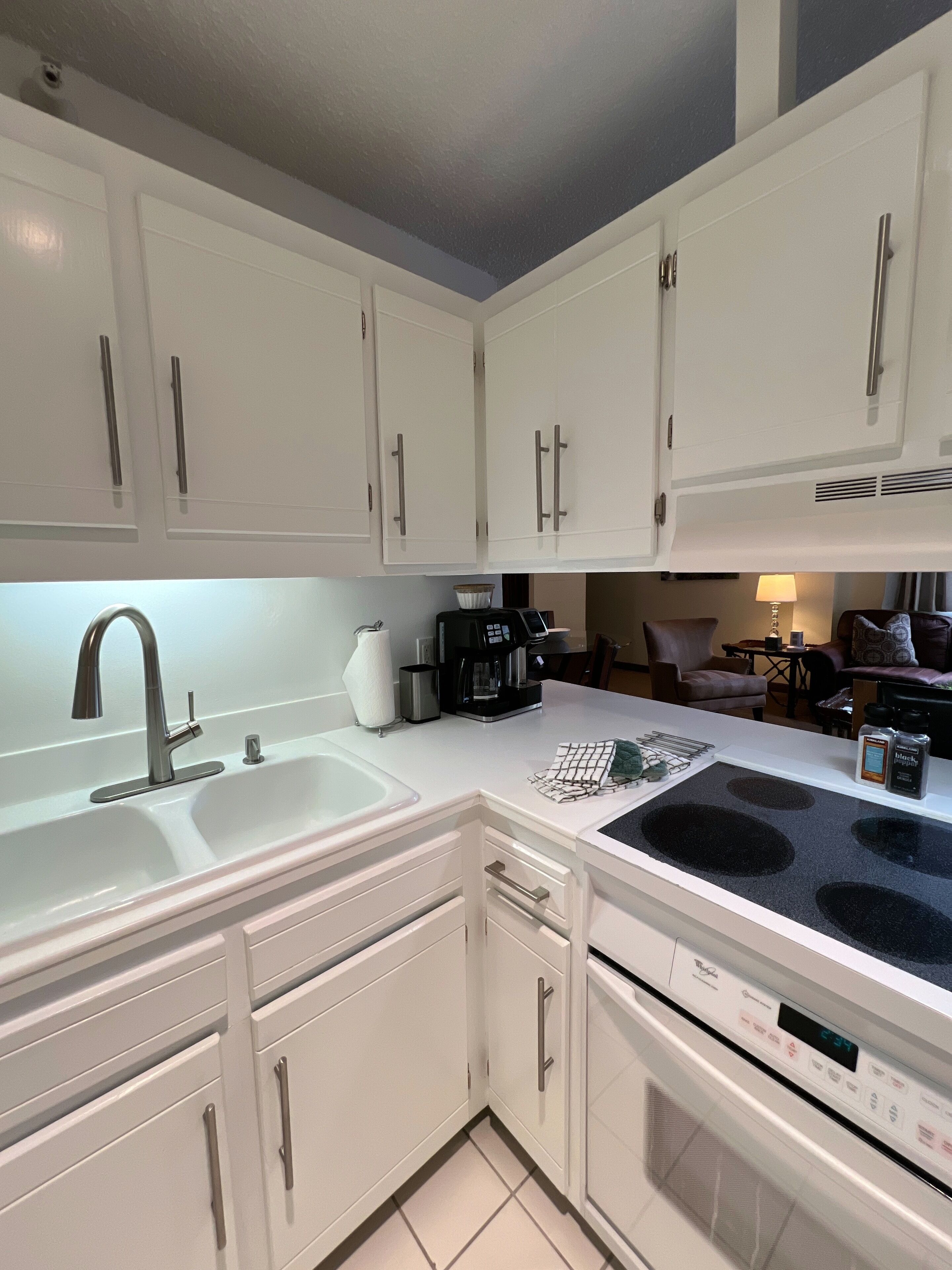 A modern kitchen with white cabinets, a stainless steel sink, a coffee maker, and a built-in oven.