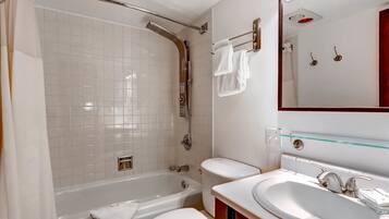 A modern bathroom with a bathtub, toilet, and sink, featuring white tiles and a glass shelf.