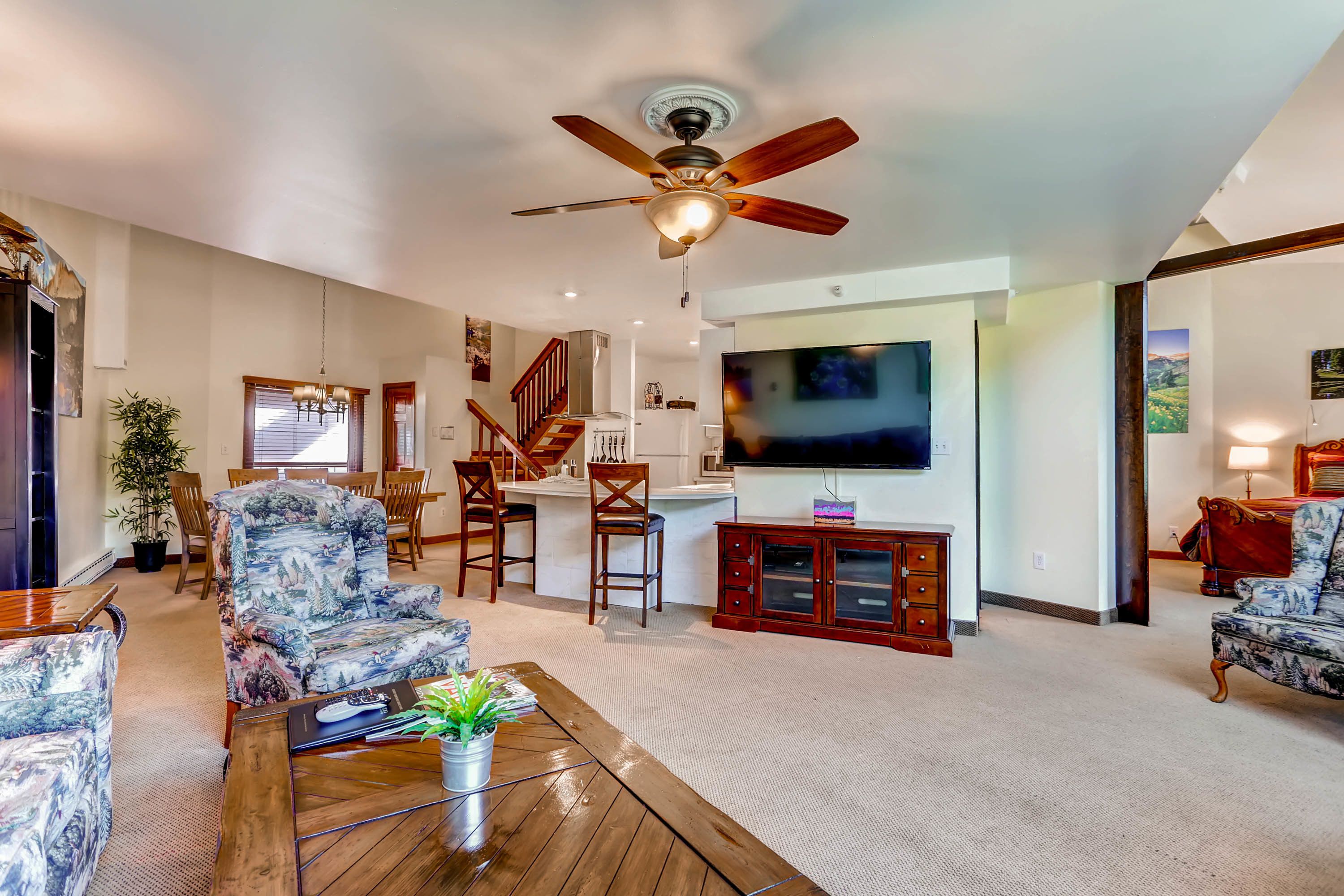 A spacious living room with a ceiling fan, a large TV, and a dining area with wooden chairs and a table.