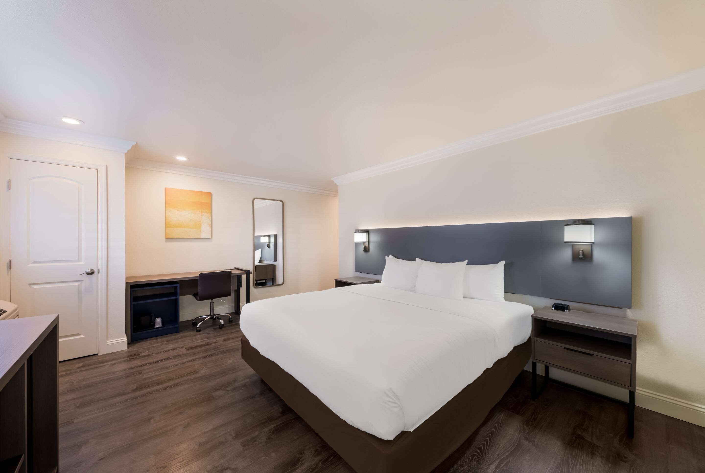 Una habitación de hotel con una cama grande, un escritorio, una silla, una mesita de noche y una lámpara de pared.