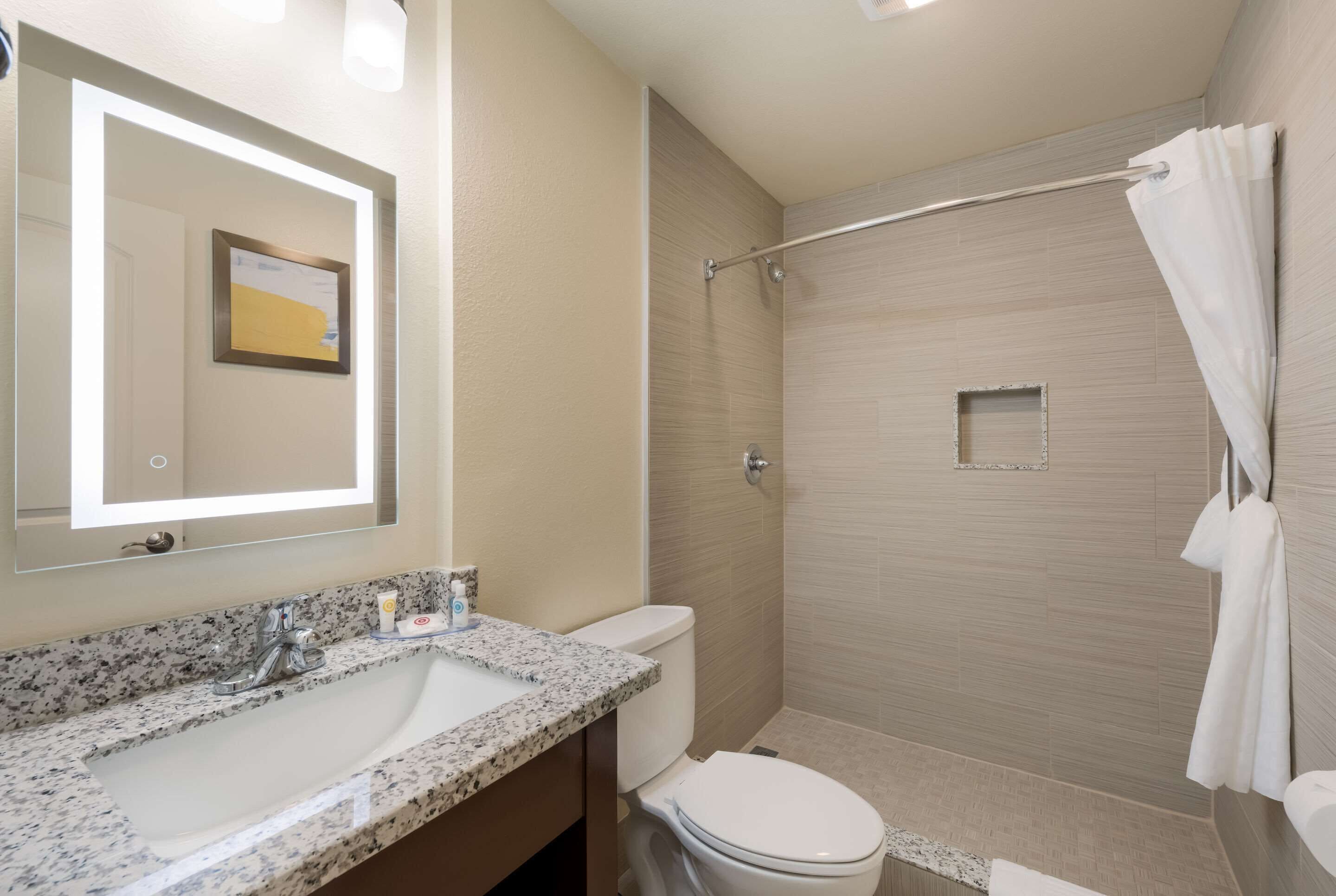 A bathroom with a granite countertop sink, a toilet, and a shower area with a glass door.