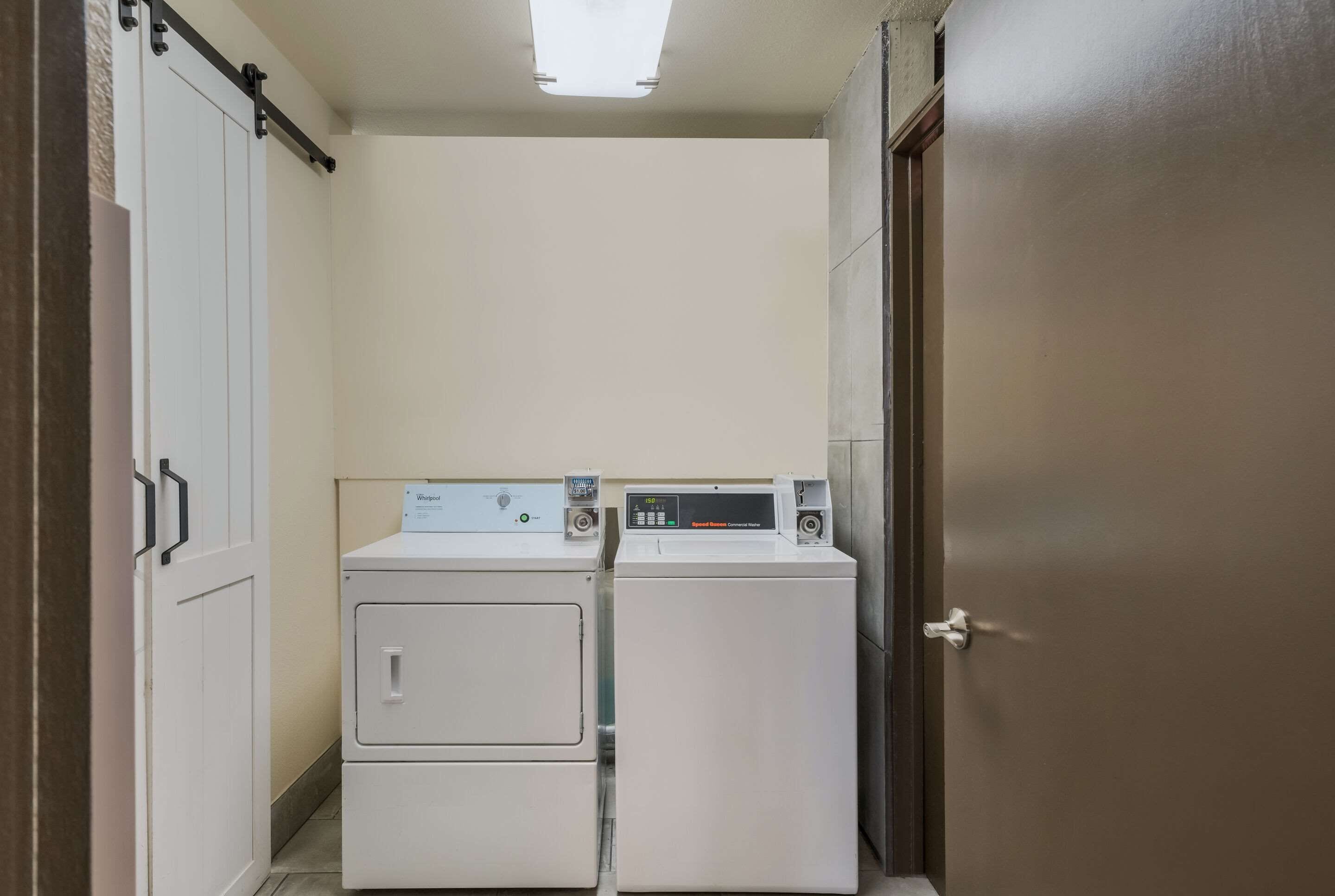 Une buanderie équipée de deux machines à laver et deux sèche-linge superposés, une porte coulissante et un luminaire au plafond.