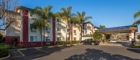 Un hotel con aparcamiento, palmeras y un panel solar en el techo.