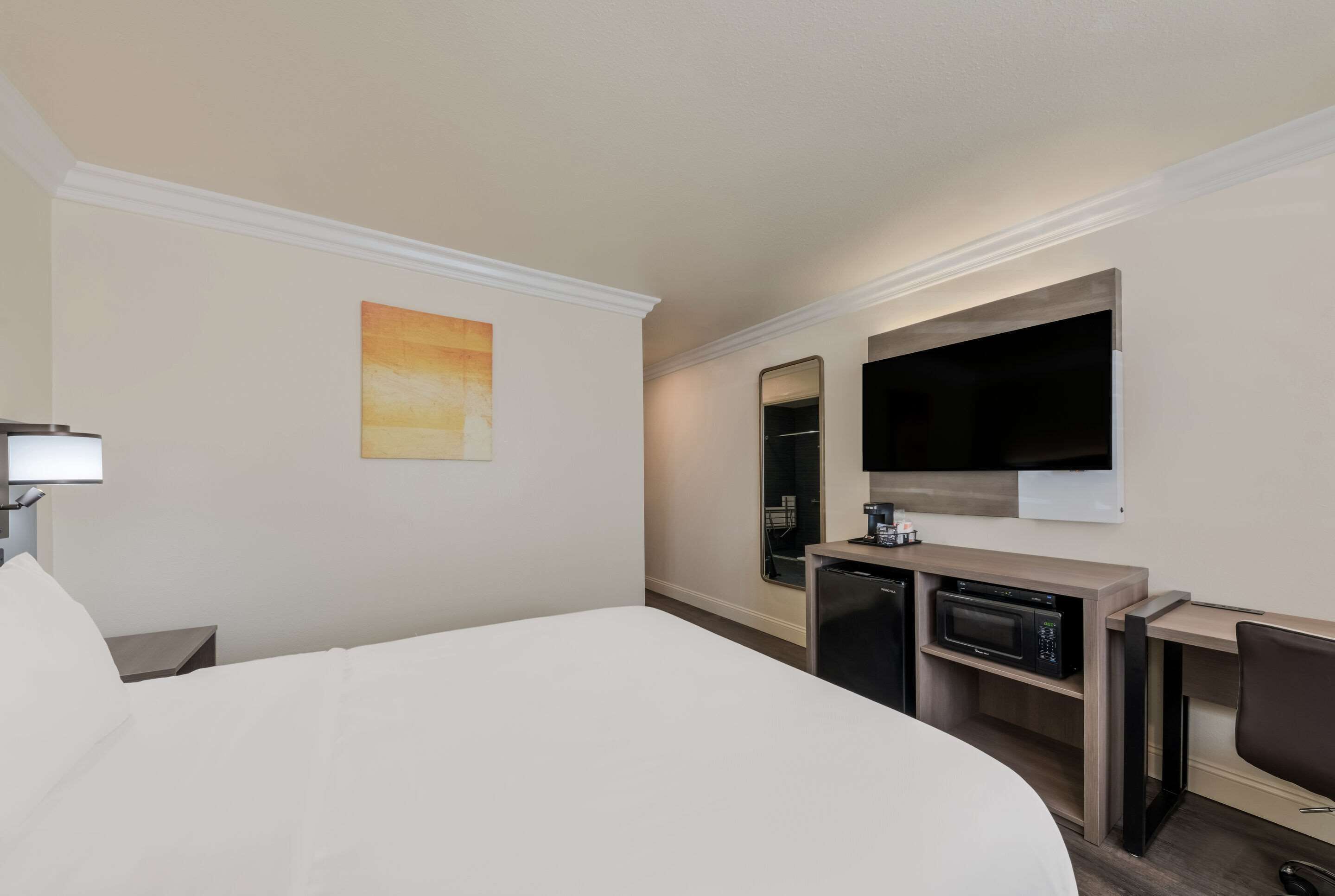 Una habitación de hotel con cama, escritorio con microondas, televisión y un cuadro en la pared.
