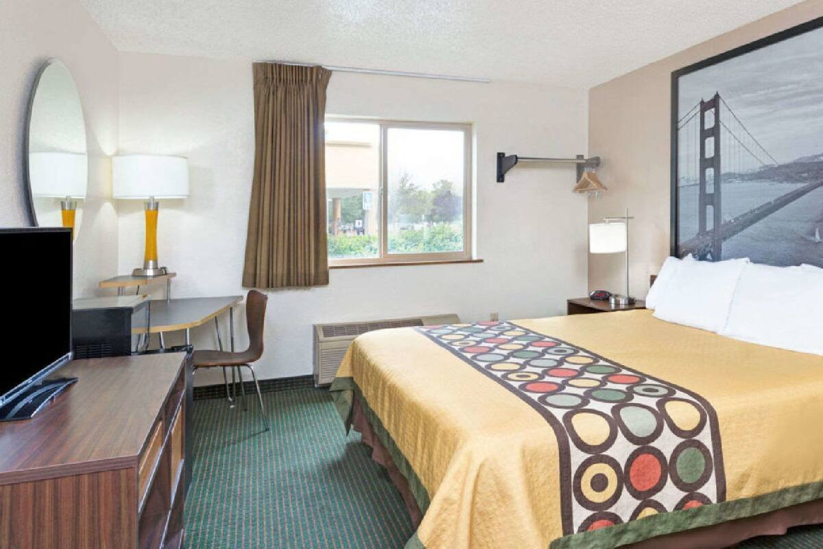 A hotel room with a bed, desk, chair, television, and a large window with a view of a bridge.