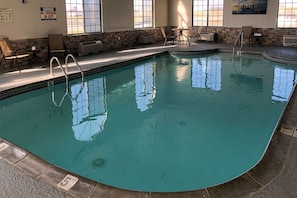 An indoor swimming pool with clear water, a lifeguard warning sign, and a stone wall.