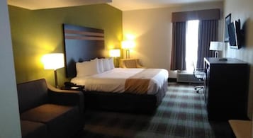 Una habitación de hotel con una cama, dos lámparas de noche, un escritorio con ordenador y un televisor en la pared.