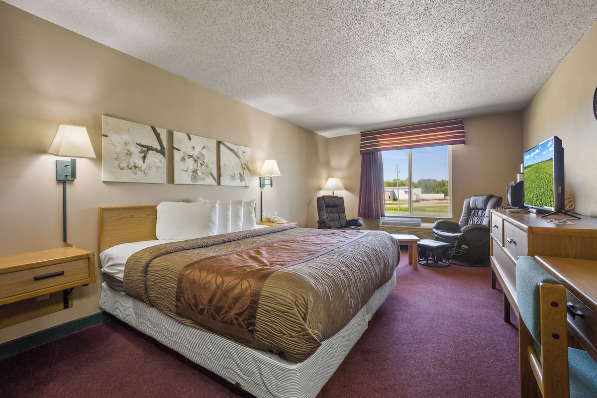 A hotel room with a large bed, a desk with a computer, a chair, a TV, and artwork on the walls.