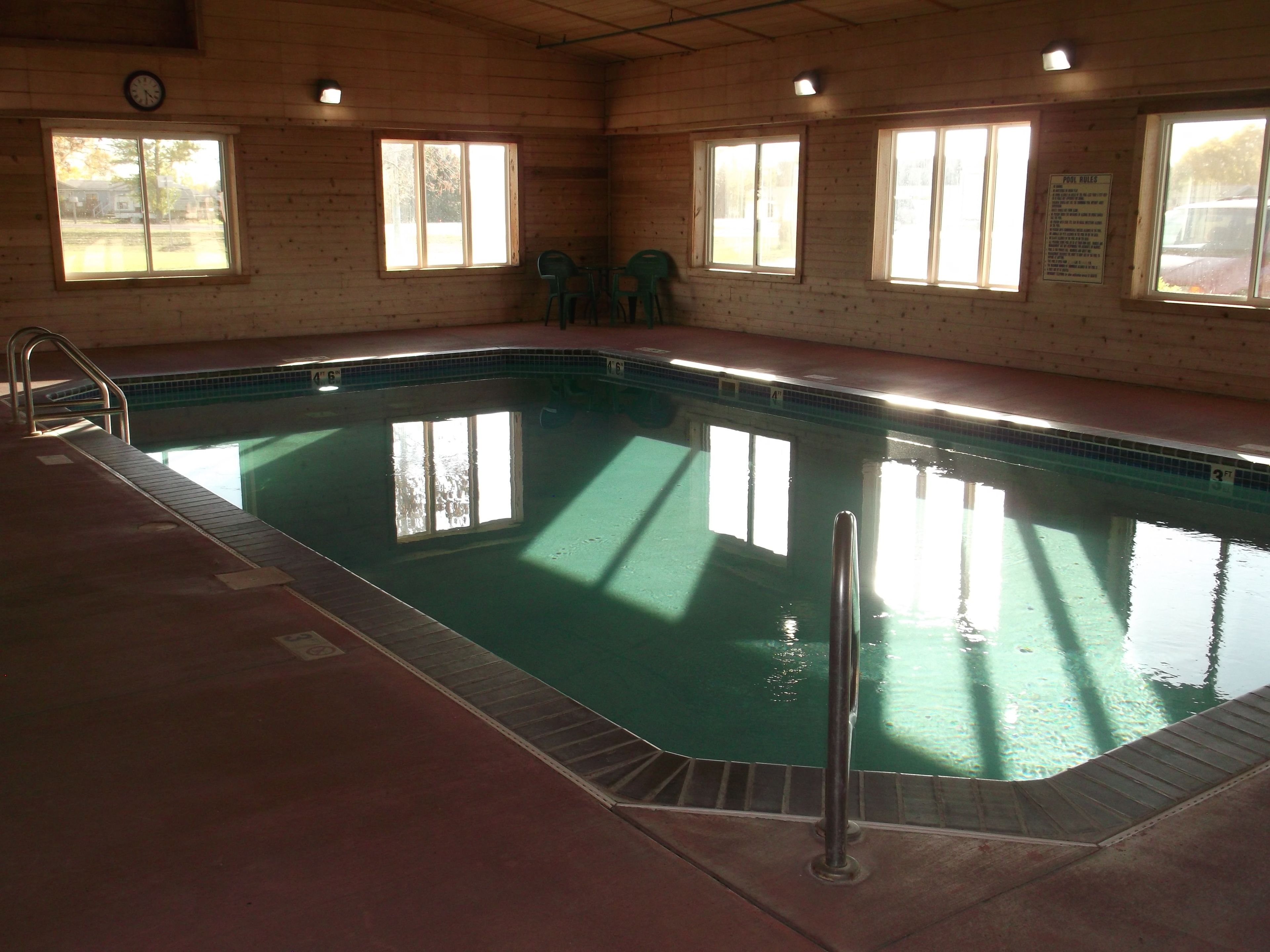 Une piscine avec un escalier, une horloge au mur et des fenêtres donnant sur l’extérieur.