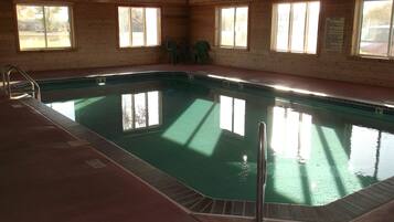 Une piscine avec un escalier, une horloge au mur et des fenêtres donnant sur l’extérieur.