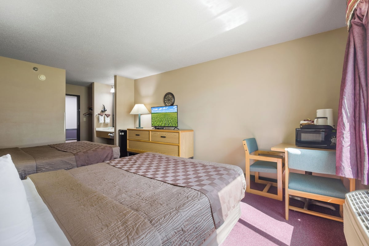 A hotel room with two beds, a desk with a chair, a television, a microwave, and a lamp.