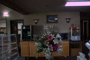 A kitchen area with a microwave, refrigerator, and a cabinet. There is a vase with flowers on the counter.